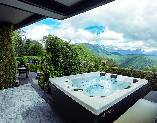 Whirlcare Whirlpool Magic Softub Schweiz in anthrazit auf einem Gartensitzplatz mit Blick aufs Land und in die Berge.